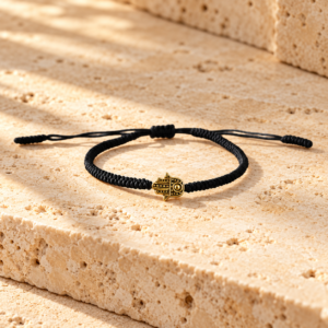 Black braided Tibetan bracelet with gold Hamsa charm on natural travertine stone